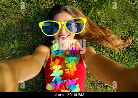 Ragazza prendere autoritratto dopo festa di Carnevale. Giovane donna selfie  con grandi divertenti occhiali da sole e garland carnevale sdraiato  sull'erba Foto stock - Alamy