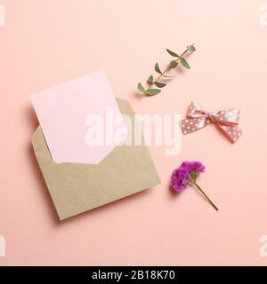Busta Kraft e carta vuota con fiore di Statice, foglie di eucalipto su sfondo rosa. Composizione floreale, disposizione piatta, vista dall'alto, spazio di copia Foto Stock