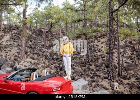 Giovane donna elegante che viaggia in auto, godendo di bei paesaggi mentre si trova sulla strada nella foresta. Stile di vita spensierato e concetto di viaggio Foto Stock