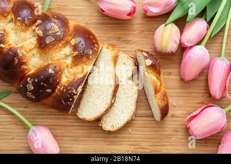 Pane dolce di Pasqua, tsoureki coconac affettato su sfondo tavola di legno, decorazione tulipani rosa, vista dall'alto. Tempo di Pasqua, primavera Foto Stock