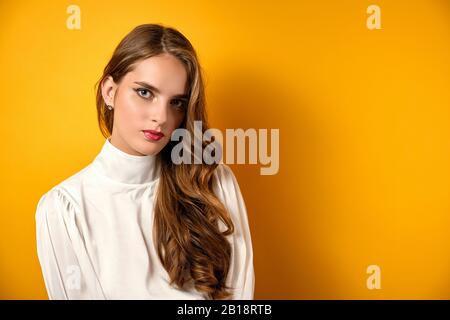 Bellissima ragazza con la pelle pulita, riccioli e rossetto rosso sorge su uno sfondo giallo. Foto Stock