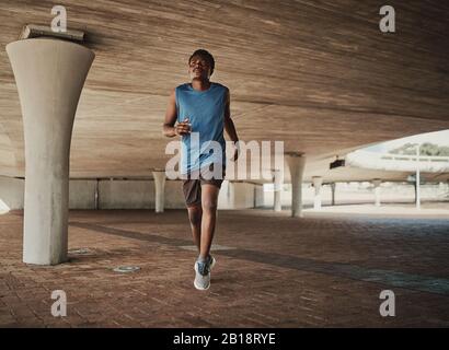 Atletica che corre al mattino sotto il ponte di cemento sul marciapiede Foto Stock