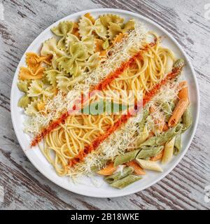 Diversi tipi di pasta in un piatto bianco su sfondo grigio di legno. Vista dall'alto Foto Stock