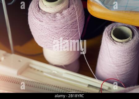 Due coni di carta con filo di lana di seta viola rosa cashmere sul tavolo e attrezzatura per maglieria. Fai-da-te hobby artigianale sfondo artigianale. Creativo Foto Stock