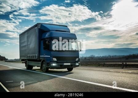 Camion semi-rimorchio blu su un'autostrada che guida al tramonto luminoso e soleggiato. Veicolo di trasporto Foto Stock