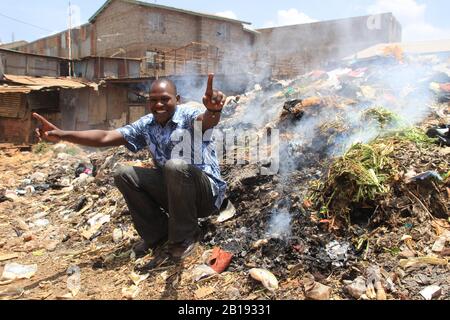 Kibera, Nairobi, Kenya - 13 febbraio 2015: Il giovane africano si siede e sorride su una montagna di spazzatura Foto Stock