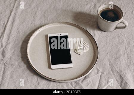 Una tazza di caffè e un bigliettino vuoto, invito su piastra in ceramica. Moody colazione tavolo mockup scena. Tovaglia di lino beige sullo sfondo. Sparse Foto Stock