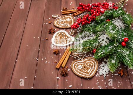 Sfondo di Natale. Capodanno abete, rosa canina, foglie fresche, uncinetto zenzero biscotti cuori, spezie e neve artificiale. Sfondo tavole di legno, Foto Stock