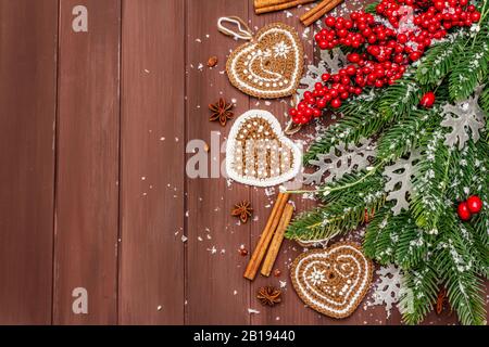 Sfondo di Natale. Capodanno abete, rosa canina, foglie fresche, uncinetto zenzero biscotti cuori, spezie e neve artificiale. Sfondo tavole di legno, Foto Stock