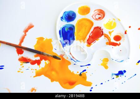 Sul tavolo bianco c'era un pasticcio creativo - c'è una tavolozza di plastica su cui si mescolano i colori, un pennello per disegnare e vernici di colore diverso Foto Stock