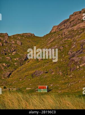 Al di là del machair una piccola cappella alla base di una montagna rocciosa sopra la remota Baia di Sanna al tramonto, Penisola di Ardnamurchan, Scozia Foto Stock