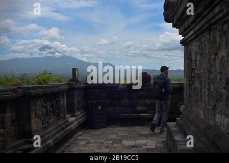 Giovane uomo cammina sulla storia del tempio di Borobudur, con vista sulla montagna sullo sfondo. Foto Stock