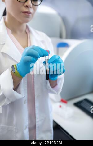 Medico dai capelli scuri in un accappatoio bianco che tiene in mano una provetta Foto Stock