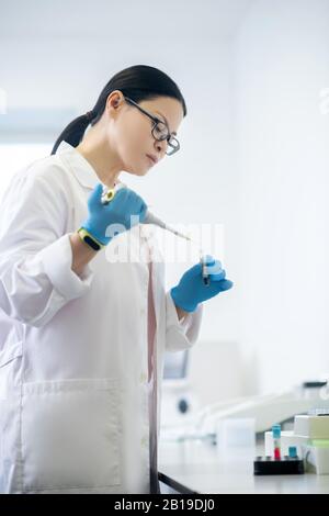 Il tecnico deve indossare guanti di colore blu che versare il campione di sangue nella provetta e guardare concentrato Foto Stock