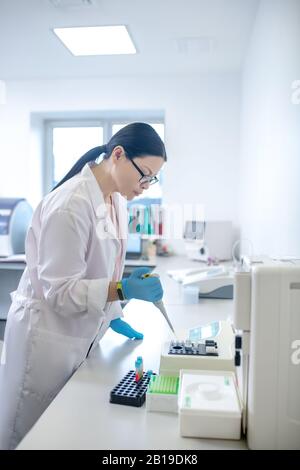 Il tecnico deve indossare guanti di colore blu per versare il campione di sangue nella provetta Foto Stock