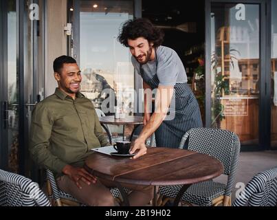 Allegro giovane uomo che serve un cliente afro-americano alla caffetteria Foto Stock