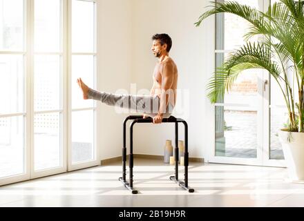 Fit uomo muscolare fare V Sit calisthenics esercizi su barre parallele per tonificare e rafforzare i suoi muscoli in una luminosa palestra ariosa con spazio di copia in una guarigione Foto Stock