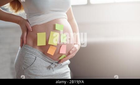 Concetto di scelta del nome del bambino. Scatto corto della donna incinta con gli adesivi vuoti della carta sul pancino, primo piano. Inserire il testo. Copyspace Foto Stock