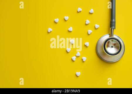 Stetoscopio medico e pillole di cuore bianco su sfondo giallo salute minimalismo concetto Foto Stock