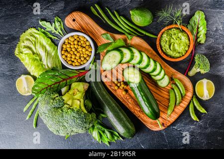 Verdure assortite a disposizione piatta con tonalità verdi su tavola scura, vista dall'alto del concetto di cibo crudo biologico fresco. Foto Stock