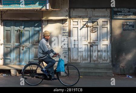 Jamnagar, Gujarat, India - Dicembre 2018: Un uomo passa in bicicletta attraverso i negozi in navata nelle strade del mercato in una vacanza. Foto Stock