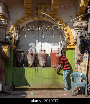 Junagadh, Gujarat/India - 7 dicembre 2018: Un uomo riempie un bicchiere d'acqua dalle pentole d'acqua di argilla nella strada principale del mercato. Foto Stock