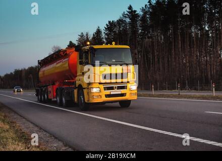 Un camion trasporta un serbatoio di combustibile su un'autostrada contro una foresta e un cielo blu. Il concetto di trasporto di merci pericolose su strada Foto Stock