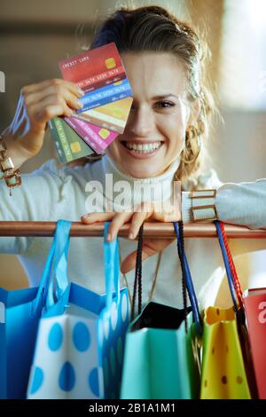 felice femmina alla moda in maglione bianco e gonna vicino borse colorate shopping appesi su barra di rame vestiti con un ventilatore di carte di credito. Foto Stock