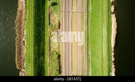 Linee ferroviarie. Vista aerea verticale del drone di una coppia di binari ferroviari delimitati da acqua e percorsi che creano texture astratte allineate. Foto Stock