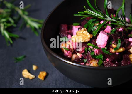 Insalata di barbabietole con formaggio feta e noci disposte in una ciotola di ceramica marrone su ardesia nera decorata con prezzemolo Foto Stock