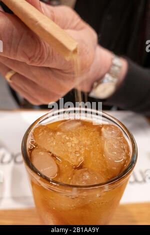 Uomo che aggiunge zucchero ad un bicchiere di tè freddo senza dolcificanti con cuneo di limone Foto Stock