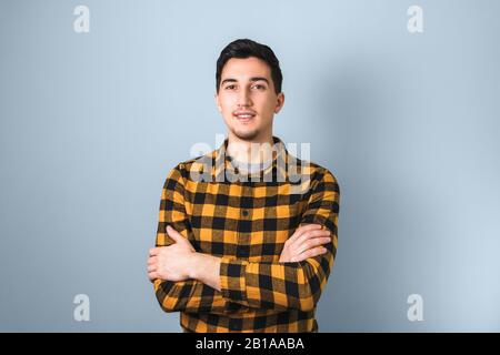 bel ragazzo in camicia quadrata gialla con braccia incrociate su sfondo azzurro Foto Stock