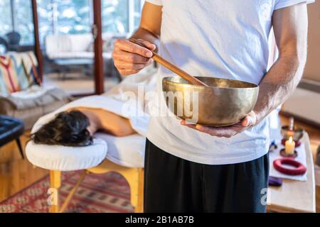 Uomo che tiene una ciotola di suono di bronzo con un bastone - usato per la terapia del suono e massaggi sonori. Un massaggiatore professionale che offre un massaggio sano Foto Stock