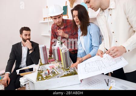 quattro architetti che si trovano attorno al tavolo per una riunione. primo piano vista laterale foto Foto Stock