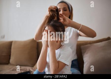 la ragazza non vuole che i capelli siano spazzolati. primo piano foto. capretto si sente male, perché la madre tira i capelli, capretto coprendo il viso con le palme, le mani Foto Stock