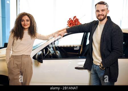 Giovane coppia amorevole in piedi di fronte alla loro nuova automobile Bel ragazzo e sua moglie acquistare nuova auto al concessionario.happiness, meglio presente su bi Foto Stock