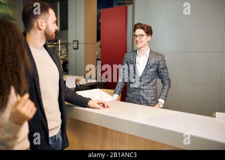 giovane ed elegante venditore che parla con una giovane coppia alla fiera della concessionaria show room.close up foto. lavorare con i clienti. business, lavoro, professione, occupati Foto Stock
