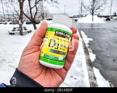 Montreal, Canada - 10 febbraio 2020: Una mano che tiene Kirkland Vitamin D Pack sopra lo sfondo del magazzino Costco. La carenza di vitamina D può causare una perdita Foto Stock