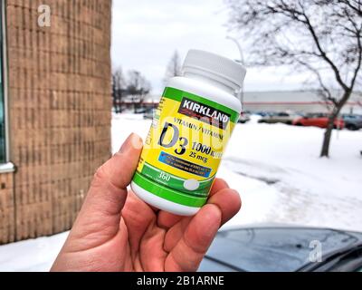 Montreal, Canada - 10 febbraio 2020: Una mano che tiene Kirkland Vitamin D Pack sopra lo sfondo del magazzino Costco. La carenza di vitamina D può causare una perdita Foto Stock