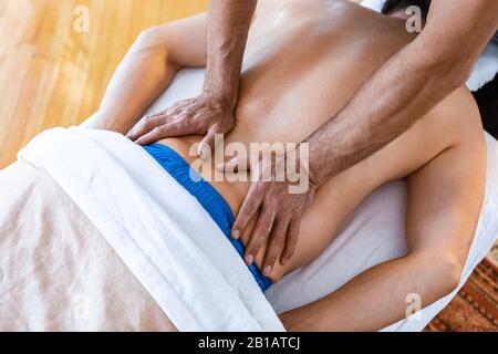 Un maschio irriconoscibile sdraiato sul tavolo e che riceve il massaggio alla schiena da un massaggiatore professionista. Vista dall'alto Foto Stock