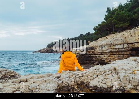 La donna posa sul bordo della scogliera alla ricerca sulle grandi onde Foto Stock