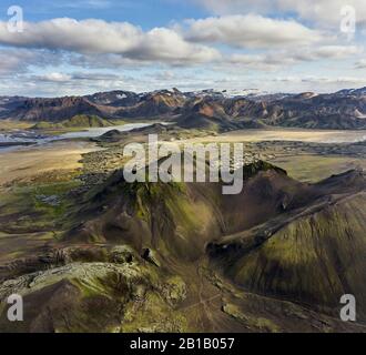 Pittoresca vista dei droni su montagne ruvide coperte di erba e muschio contro il cielo nuvoloso in Islanda Foto Stock