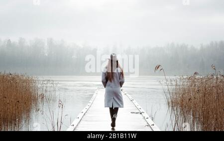 donna che cammina da sola pensando al mare in inverno su un molo Foto Stock