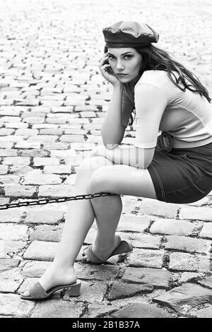 Giovane bella bruna emotional ragazza vestita rétro in stile vintage nella vecchia città europea si siede in una catena Foto Stock