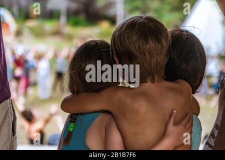 Una vista ravvicinata e posteriore di tre bambini carini, due fratelli e una sorella, abbracciando sul palco durante un festival che celebra la terra e la cultura. Fuoco selettivo Foto Stock