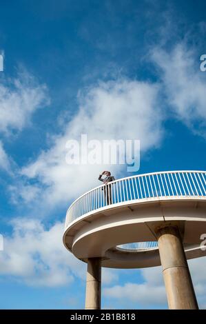 Uomo d'affari lontano in piedi all'aperto su un passaggio curvo che guarda fuori in cielo blu brillante Foto Stock