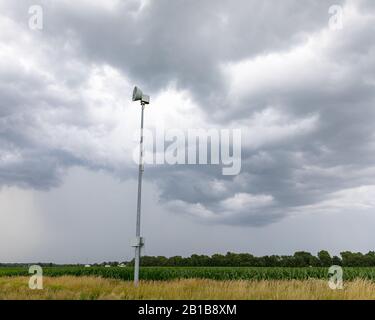 Grave allarme meteo e sirena di tornado lungo la strada rurale con nuvole buie tempesta e pioggia in background Foto Stock