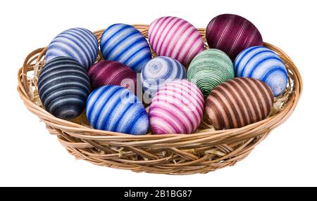 Uova di Pasqua a righe decorate a mano in cesto di vimini isolato su sfondo bianco. Gusci d'uovo vuoti colorati avvolti da filo di cucitura di cotone sottile incollato. Foto Stock