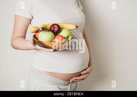 Pancia incinta, donna con cibo sano, ciotola di frutta in mano. Spazio di copia. Foto Stock