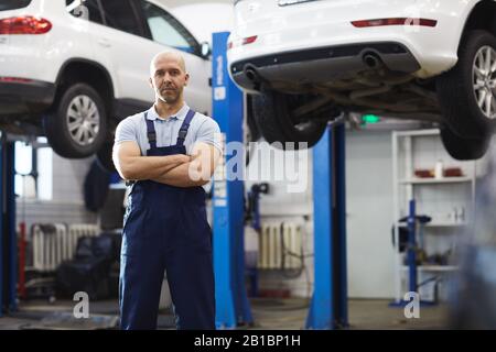 Ritratto di meccanico muscolare auto in piedi con le braccia incrociate mentre posa in garage, copia spazio Foto Stock